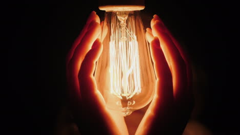 back view of man warms his hands near a light bulb in the dark