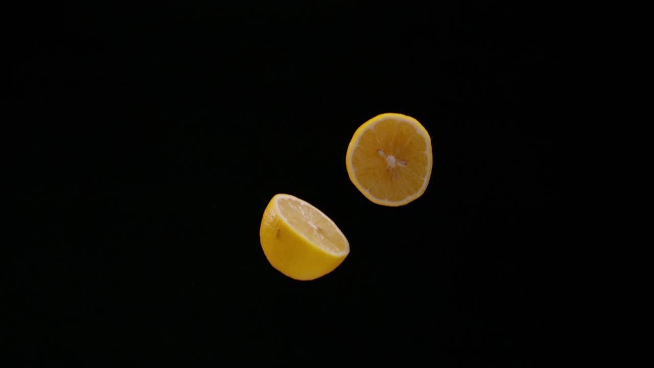 Cut in half lemon falling down isolated on black background, slow motion
