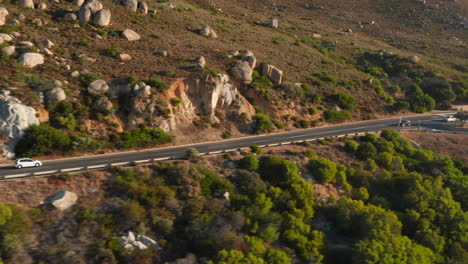 white car driving at victoria road passing by mountain hills with boulders in south africa