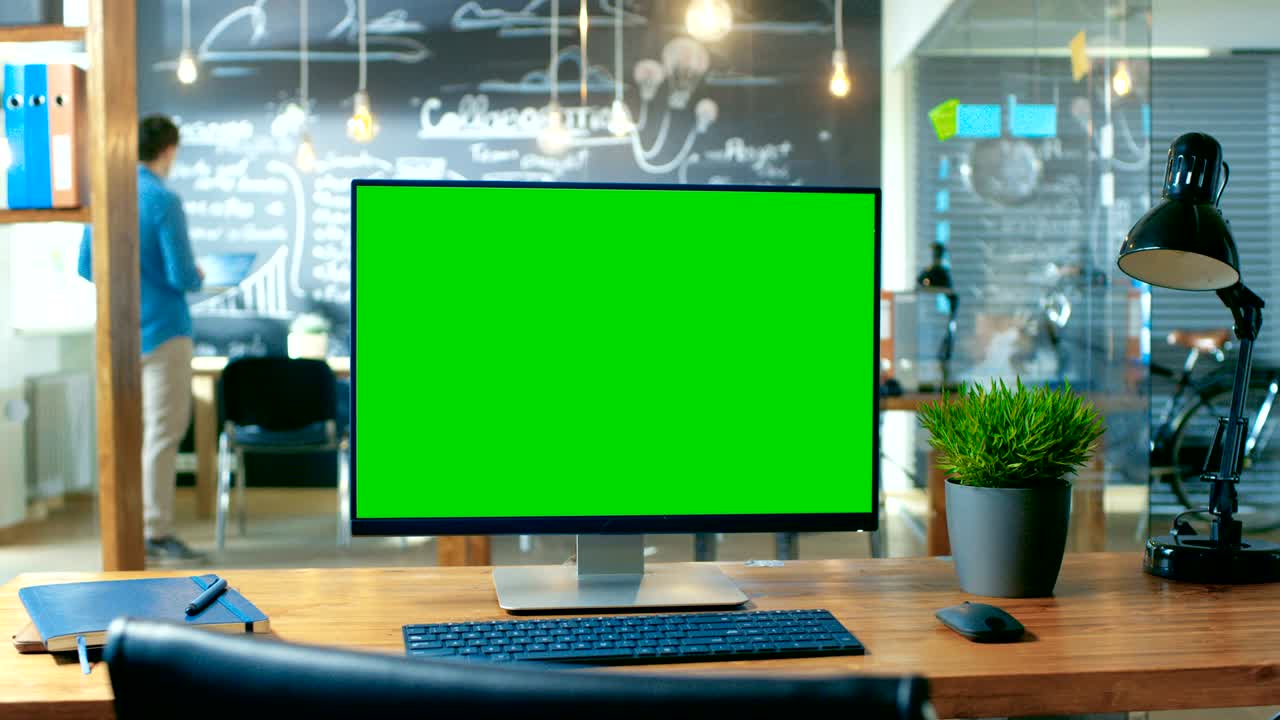 un computer personale con un monitor a schermo verde sta sulla scrivania dell'ufficio. sullo sfondo un uomo lavora nell'ufficio creativo di giorno.