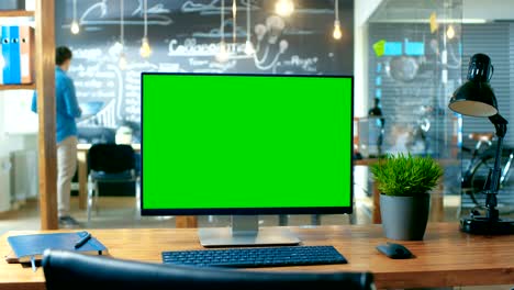 computadora personal con modelo de monitor de pantalla verde se encuentra en el escritorio de la oficina. en el fondo el hombre trabaja en la oficina creativa durante el día.