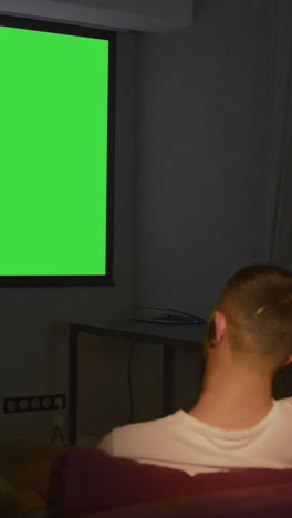 man watching a movie on a green screen projector in his home theater at night