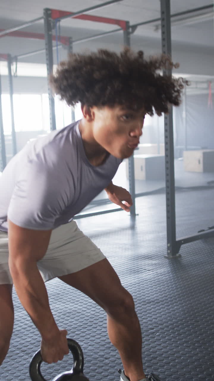 Vertical video: Lifting kettlebell, man exercising in gym, focusing on strength training