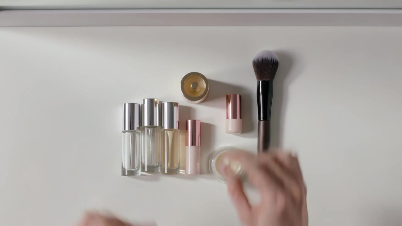 Entering bare hands arranging roller bottles, brush on vanity by mirror, inspecting open cream jar