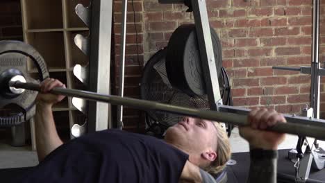 muscly man in home gym exercising barbell bench press