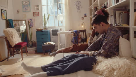 young couple resting in cozy room and using laptop on bed