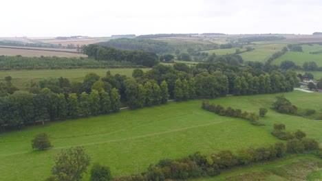 Slow-moving-drone-footage-showing-countryside,-fields-and-trees-then-panning-to-show-a-small-rural-countryside-village,-farm-and-church-in-Yorkshire,-England,-UK