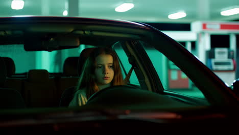 girl sitting in car at gas station at night