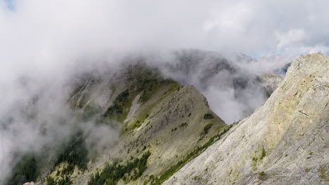 Lapso-De-Tiempo-De-Nubes-Moviéndose-Hacia-Arriba-Y-Sobre-Una-Cresta-Empinada-Con-Grandes-Montañas-En-El-Fondo