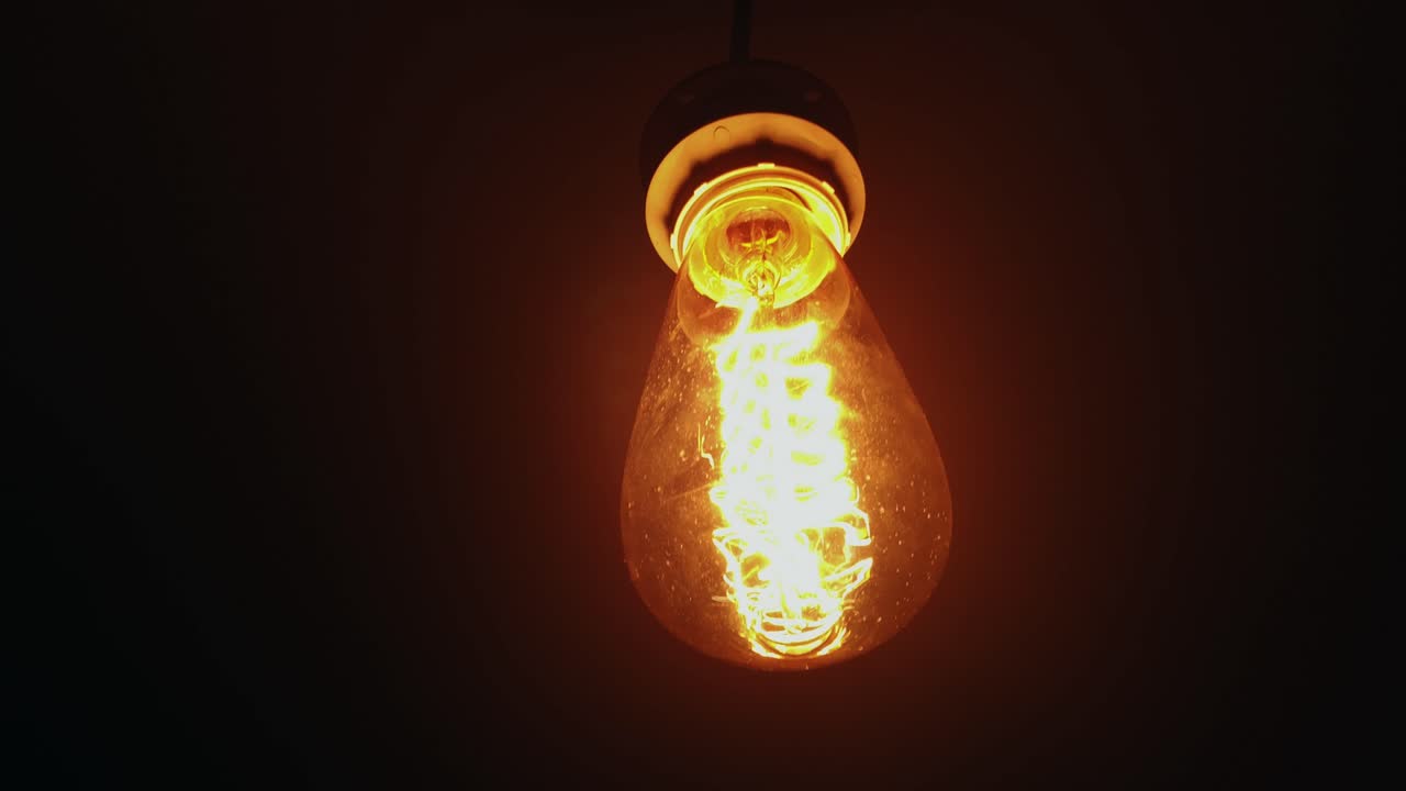 Squirrel cage incandescent light bulb hanging in the dark
