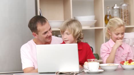 family having breakfast and using a laptop in the kitchen