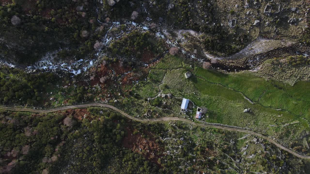 vista aérea de arriba hacia abajo de un valle de montaña verdoso con un arroyo de agua y un camino de tierra