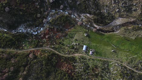 Aerial-top-down-view-of-a-greenish-mountain-valley-with-a-water-creek-and-a-dirt-road