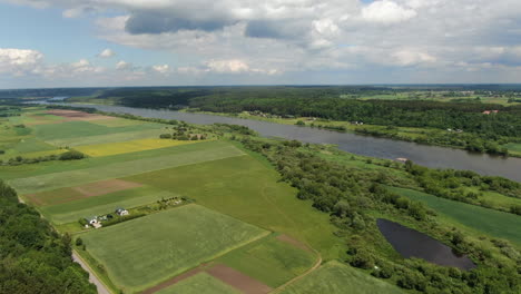 Green-vibrant-fields-and-forest-near-river-valley,-high-angle-drone-view