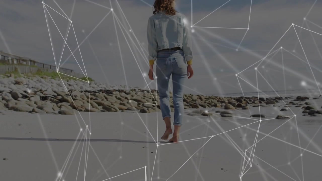 Barefoot woman pressing wet sand and walking shoreline, technology overlay expanding over beach