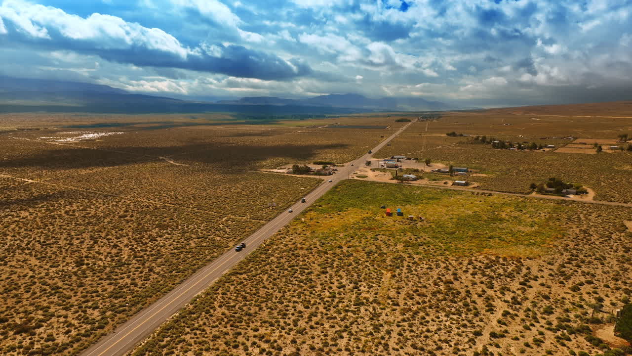 A few houses near the highway in Nevada desert. Rainy cloudscape covering the sky above the landscape. Aerial view.