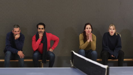 watching table tennis match, group of people sitting on bench, smiling and engaged