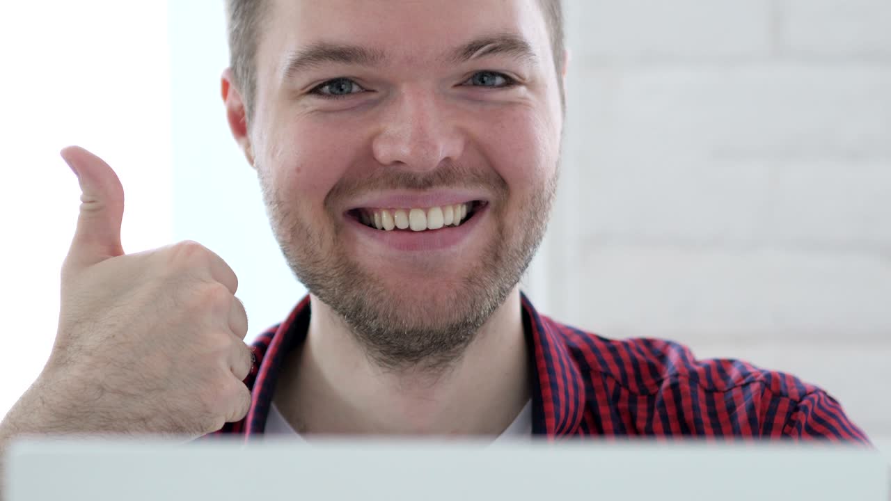 pulgares hacia arriba por un joven que trabaja en una computadora portátil