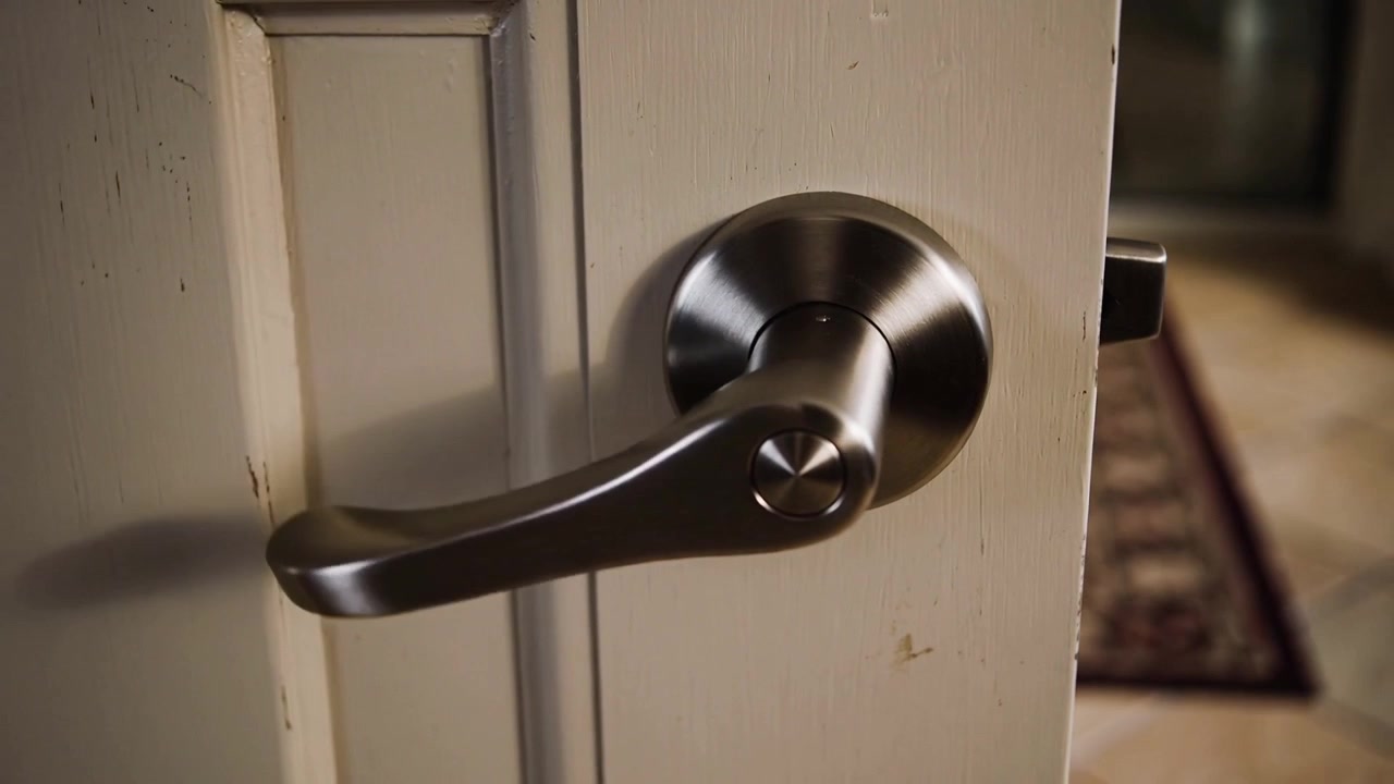 Rotating metal lever handle retracting latch and opening into tiled hallway, showing patterned rug