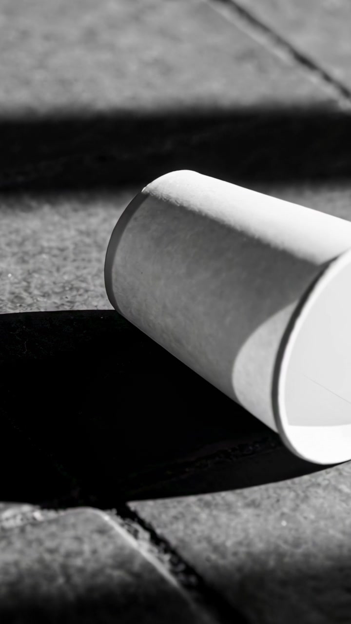 Vertical video: Rotating paper cup shifting right on pavement, showing rim and shadow, copy space