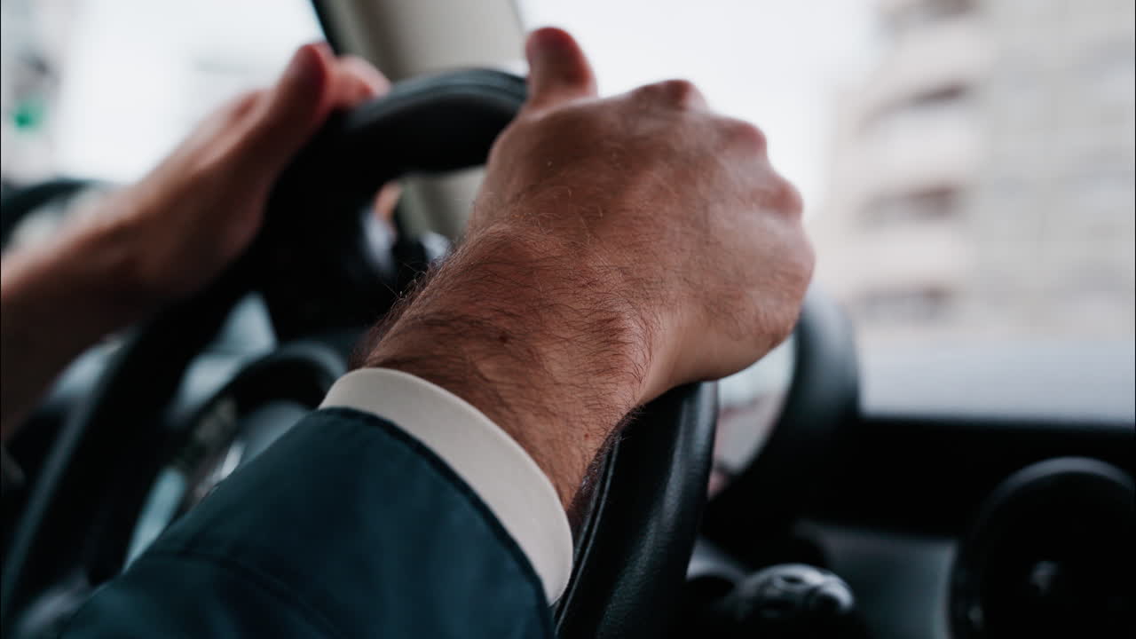Close up of a man's hands on a steering wheel, driving a car on the road