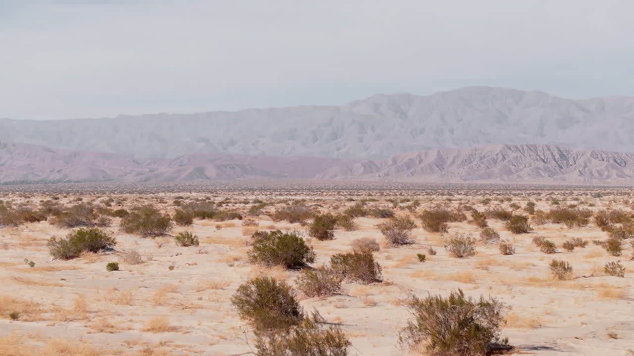 Stretching vistas of the Barstow desert showcase a serene natural landscape. The dry terrain features scattered shrubs and distant mountains, creating a tranquil and timeless atmosphere