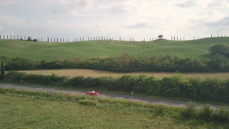 Roter-Oldtimer-Von-Fabrizio-Fährt-Entlang-Der-Cypress-Hill-Road-In-Der-Toskana,-Italien,-Luftdrohne-Folgt