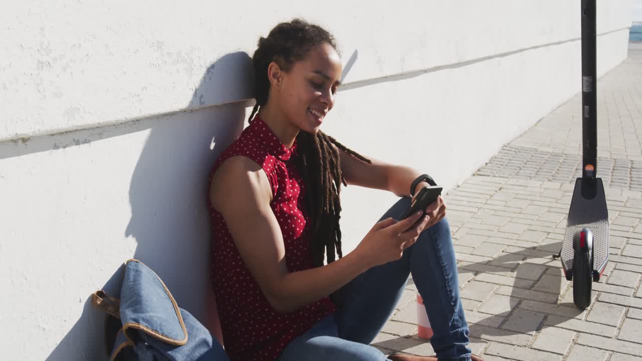 African american woman sitting and using smartphone on promenade by the sea