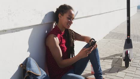 African-american-woman-sitting-and-using-smartphone-on-promenade-by-the-sea