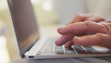 cerca de las manos de una mujer caucásica mayor escribiendo en una computadora portátil