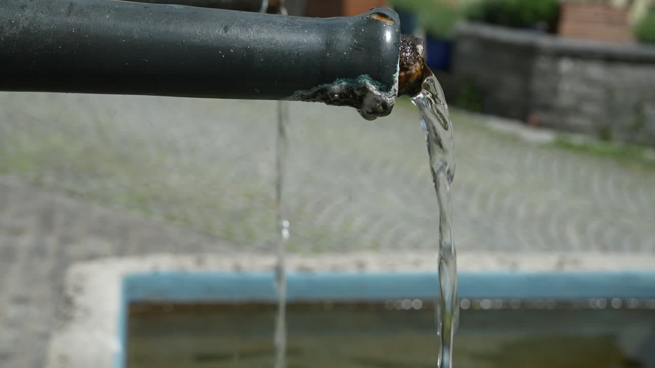 Clear water splashes out of a rustic, metal pipe fountain in Walenstadt, Switzerland, a fresh water source. A traditional or public water point, emphasizing simplicity and functionality