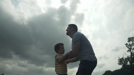 a happy, loving father holding and hugging his son for a warm, positive family moment outside under the sunlight shines through clouds.