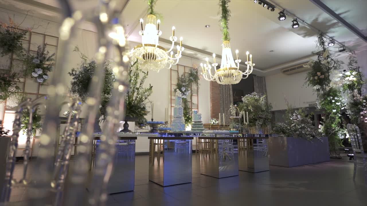 Revealing footage of elegant white room with chandeliers, glass tables, and floral arrangements for a Sweet Fifteen birthday celebration
