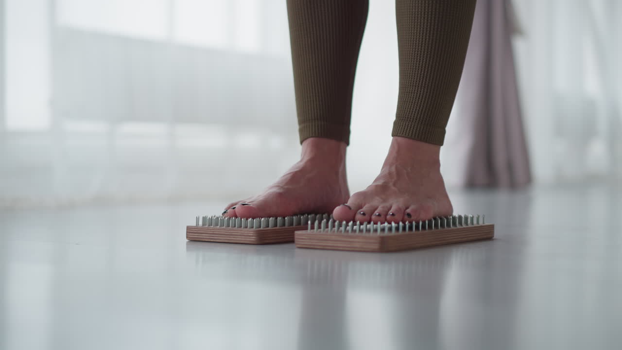 Leg view disciplined practitioner stands barefoot on nail mat in bright studio focusing on grounding and resilience under soft ambient light with black painted toenails showcasing resilience