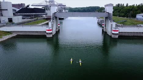 Aerial-footage-of-Kayak-and-Canoe-paddlers-on-a-green-river-in-Germany-paddling-under-bridge-un-a-harbour