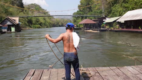 a man is working with some ropes and sailing on the river of sai yok on a floating house, in the jungle of thailand