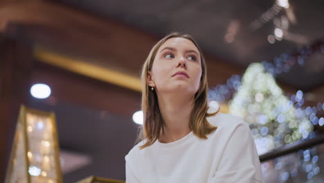 lady looking around contemplatively in festive indoor setting with blurred background featuring decorative lights and bokeh with warm ambient lighting