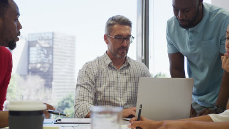 Diverse-male-and-female-business-colleagues-talking-and-using-laptop