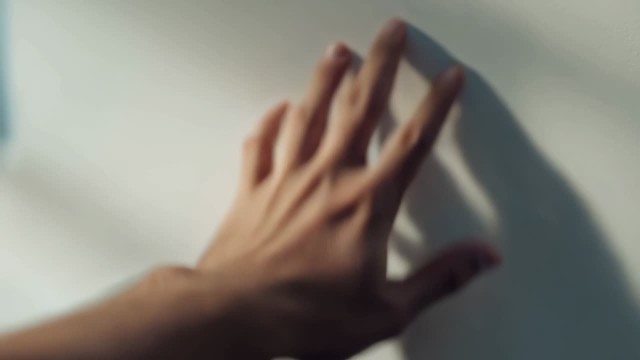 Man reaching from lower left and pressing palm against light wall, feeling texture under fingers