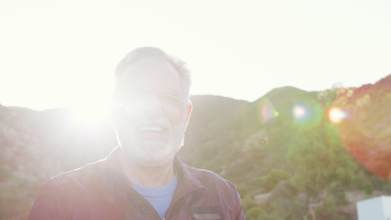 Portrait Of Smiling Hispanic Senior Man Outdoors In Countryside Against Flaring Sun