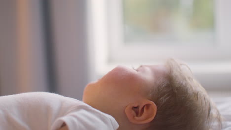 side view of a baby lying on the bed in bedroom while his mother is giving him water with the feeding bottle