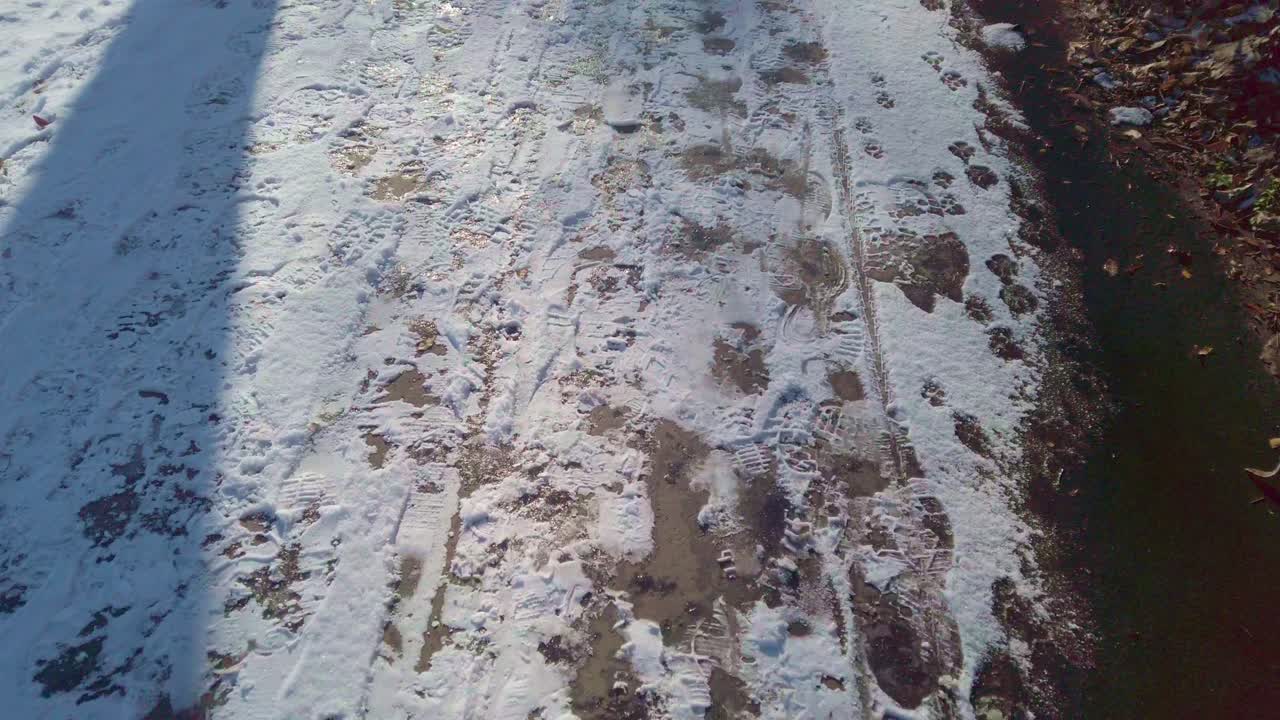 Die Ich-Perspektive der Navigation auf eisigem Pflaster. Detaillierte Ansicht von gefrorenem Wasser und Schneematsch auf dunkler Fahrbahnoberfläche, die Winterwettergefahren und rutschige Außenbedingungen einfängt
