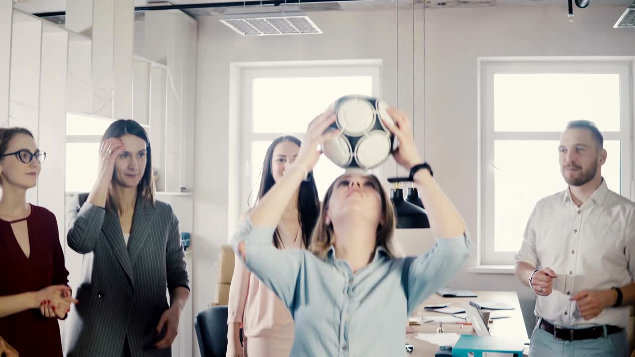 백인 소녀는 사무실에서 머리로 축구를 장난합니다. 행복한 다인종 사업가들은 일에서 성공을 축하합니다.