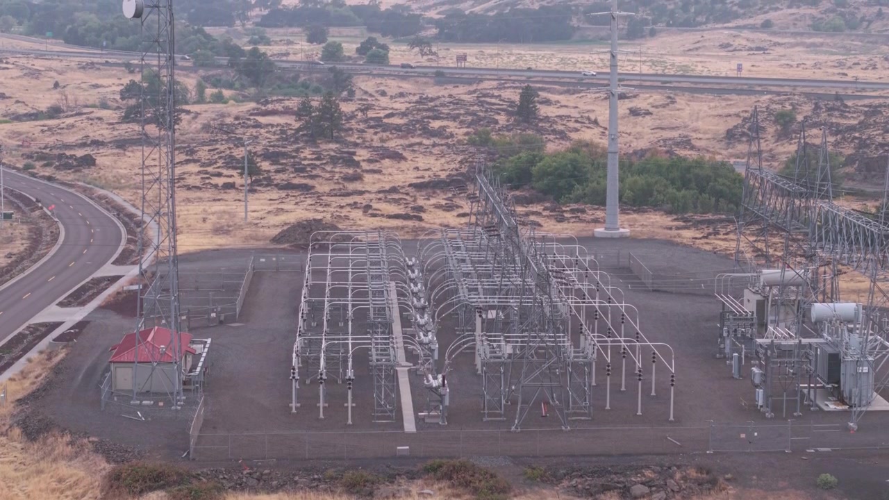 Umspannwerk in der Nähe eines Rechenzentrums in The Dalles, Oregon, mit der Interstate 84 in der Ferne über die trockene Industrielandschaft sichtbar. Drohnenaufnahme mit Aufwärtsneigung.