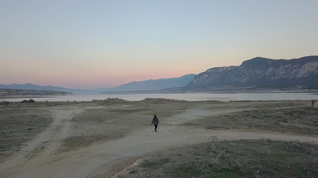 Forward drone shot of a girl running towards the lake