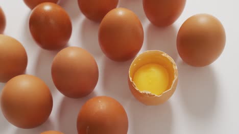 Close-up-of-half-broken-egg-with-among-other-eggs-on-white-surface