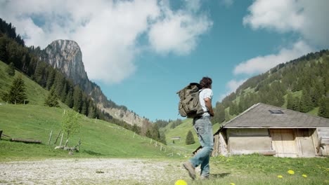 Millennial-man-in-casual-clothing-with-backpack-hiking-on-mountain-valley-path-in-slow-motion