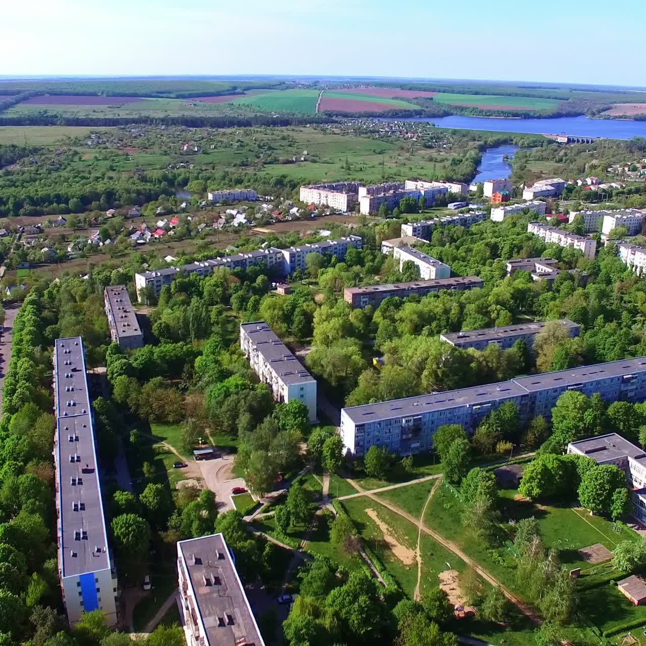 Nice green city panorama lit with bright sun on summer season. Blocks of flats drowning in the greenery. River and farmlands at backdrop