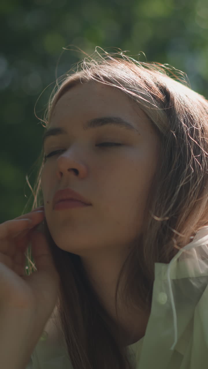 joven con impermeable translúcido baja su capucha, inclinándose hacia adelante pensativo como la luz del sol se refleja en su cara contra un fondo verde exuberante