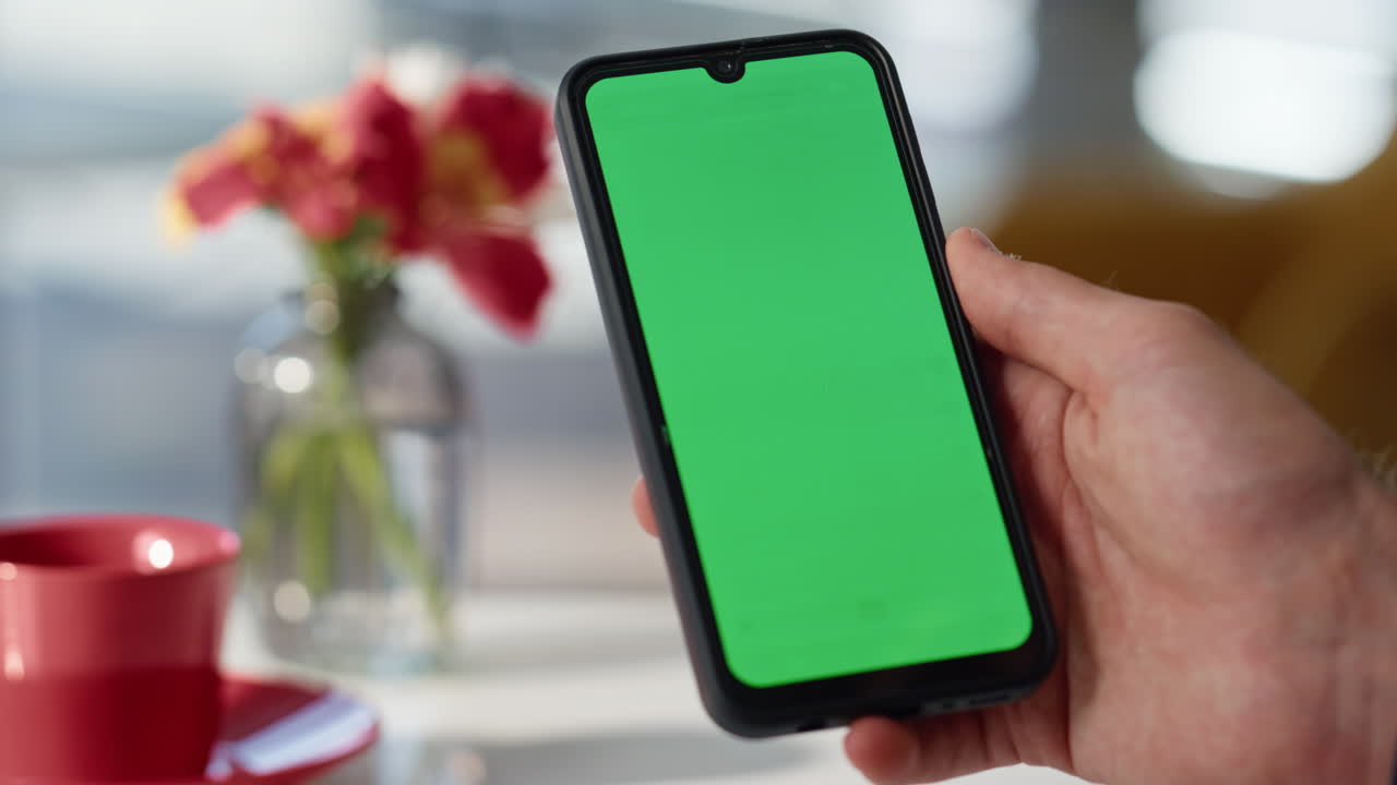 Guy finger tapping greenscreen smartphone online at coffee shop table closeup